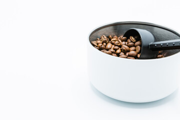 Mixture of different kinds of roasted coffee beans with black plastic spoon in white container on white background. Copy space.