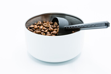 Mixture of different kinds of roasted coffee beans with black plastic spoon in white container on white background. Copy space.