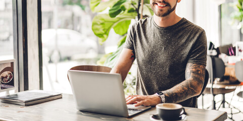 Handsome bearded hipster man use and looking at laptop computer with coffee at table in cafe.Communication and technology concept