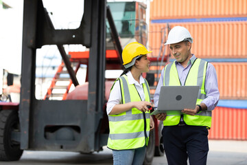 factory workers or engineers using laptop computer and talking about project work in containers warehouse storage