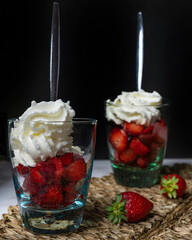 Two drinking glasses are filled with delicious strawberries and cream on a rustic straw placemat