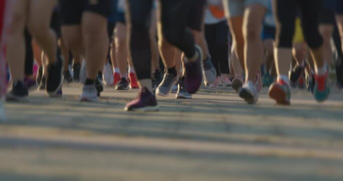Runners feet during in running marathon. Marathon athletes legs in urban city morning at sunrise, front view, zoom out, slow motion. Record 50 fps render 25 fps.