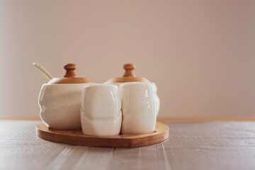 Warm colors of porcelain seasoning containers. Modern kitchenware design with wooden details. Selective focus on small containers in front, blurred background.