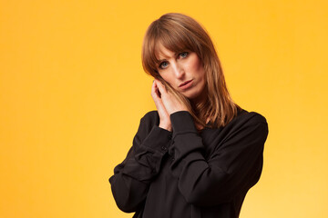 Fototapeta na wymiar Portrait of an attractive woman wearing a black long sleeve blouse against a yellow background 