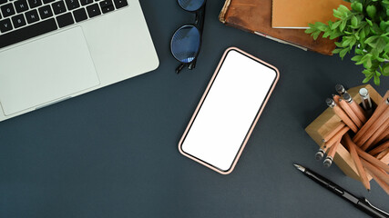 Designer workspace with smart phone, laptop, pencil holder and notebook on black holder.