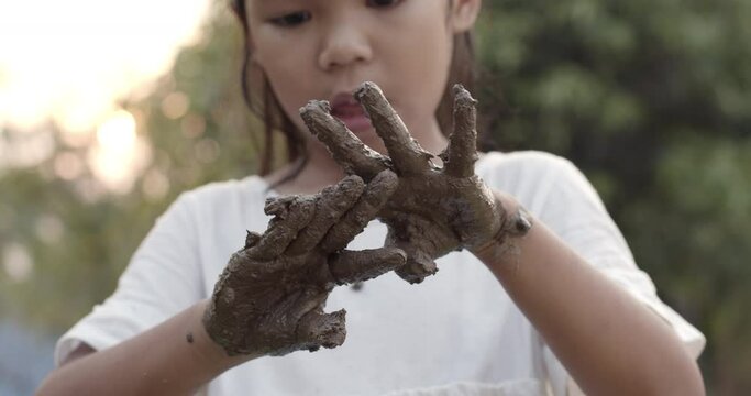 Asian child girl playing mud and showing dirty hands after planting the tree in the garden.Concept of child love in environmental conservation.Slow motion shot.