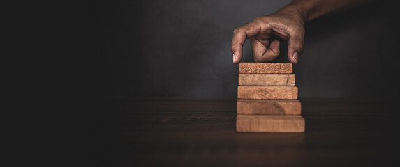 Close-up hand is placing wood block tower stacked in pyramid shape with caution to prevent collapse...