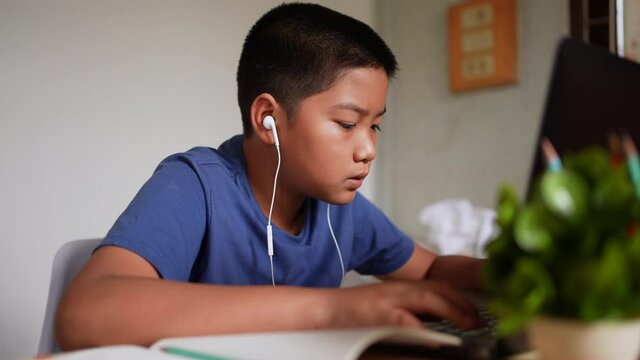 slow motion scene on asian kid boy type on keyboard laptop to do homework or listening lesson from e-learning program or surfing the internet in living room at home for lifestyle concept