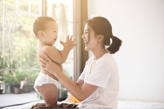 Asian mom smiling happy holding and playing with her son in living room. Mom and baby clap your hands together. Mom and baby in mother’s day concept.