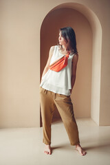 Orange Leather Crossbody Purse Small Belt Pouch Designer Belt Bag For Women. A young woman stands barefoot against the background of a beige wall. Full height.