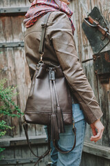 Fototapeta na wymiar Girl in a brown leather jacket and a backpack bag. Leather Backpack Purse Boho Bucket Bag Womens Convertible Backpacks. Side view.