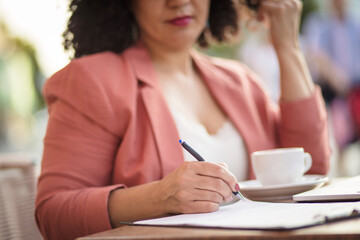 Business woman sitting in café and writing on document. Focus is on hand.