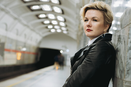 short haired caucasian woman wearing leather jacket waiting for train on platform of metro station in Saint-petersburg, Russia. Image with selective focus and noise effect
