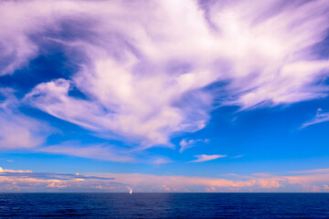 White sailboat sails on the horizon across the water on a cloudy day