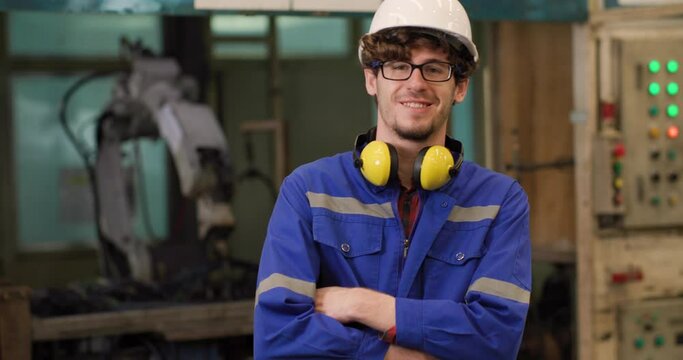 Portrait of professional industrial engineer man looking at automation robot machine and turn around to cross his arm smiling at camera in manufacturing industry. Technology and innovation concept.