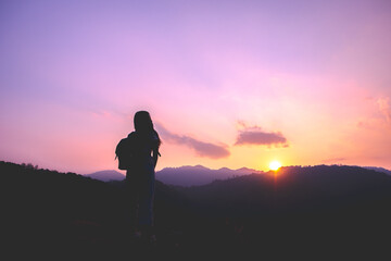 Obraz premium Silhouette of woman enjoying the sunset with dramatic sky on mountain peak.