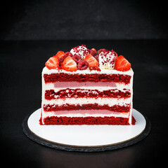 Beautiful pastries made of red velvet cake decorated with white cream, strawberries. Black background. Close-up of a red velvet cake and white cream on a white plate with a copy of the recording space
