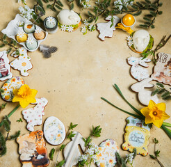 On a yellow background, Easter cakes, eggs, sweet desserts in the shape of a rabbit, flowers,green leaves of trees,willow. The items are stacked in a circle. There is a space in the middle for the tex