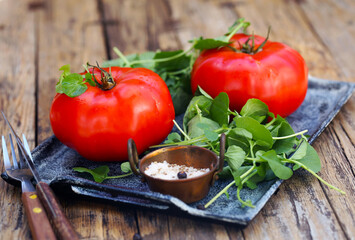 grandes tomates vermelhos maduros com salada de agrião e sal do mar estão em uma bandeja - uma...