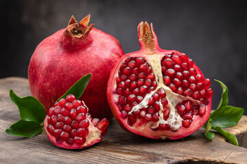 Healthy pomegranate fruit with leaves and half of ripe pomegranate on a cutting board, side view,...