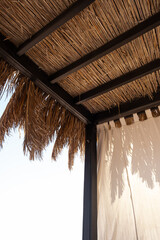 Obraz na płótnie Canvas Beautiful lounge pavilion canopy for relax on the beach with sea side view and blue sky. Tent made of dry palm leaves. Luxury summer vacation in tropical paradise resort hotel
