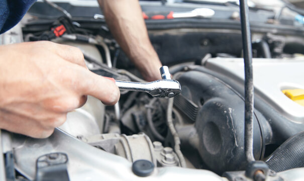 Mechanic repairing car with ratchet wrench.