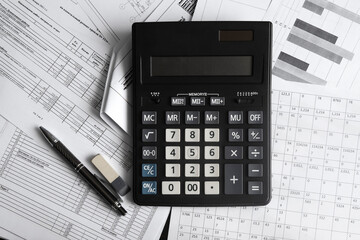 A big black calculator sits on top of a pile of working documentation. The concept of calculating funds, investments, and the family budget.