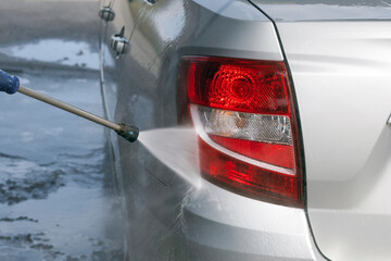 Cleaning the rear red lights of a gray car in close-up with a high-pressure washer. A stream of...
