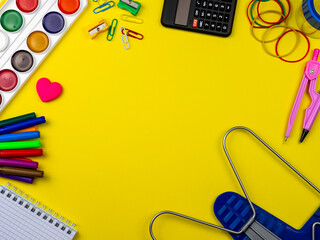 School conception, multicolored paints, pencils, markers and paper clips. School calculator and other items for the student and school on a yellow background. Flatlay, top view, copy space.