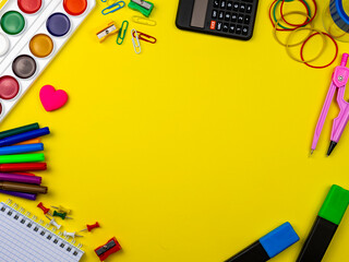 School conception, multicolored paints, pencils, markers and paper clips. School calculator and other items for the student and school on a yellow background. Flatlay, top view, copy space.