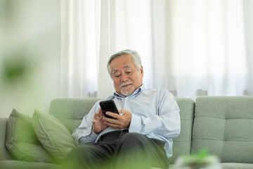 Happiness of wellness elderly asian man with white hairs sitting on sofa using mobile phone and social media smile at home,Senior lifestyle at home concept
