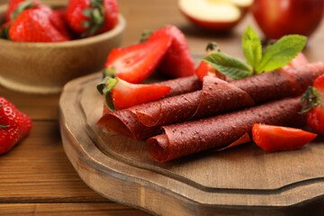 Delicious fruit leather rolls and strawberries on wooden table, closeup