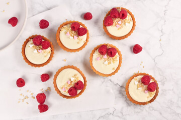 Homemade small tartlet pastries with white cream, topped with raspberry fruits and almond sprinkles