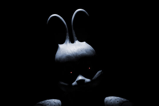 A creepy bunny looks out from the darkness. The face of a scary white toy rabbit with red eyes
