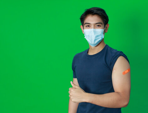 Asian young man wearing protective hygiene mask trust and confident show arms with bandage plaster after getting Coronavirus or Covid-19 vaccine injection. Idea for safe and drug allergy free