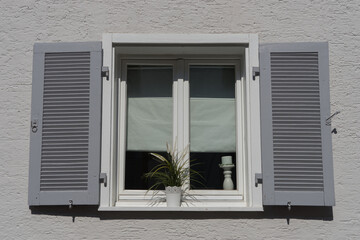 Background: old white double casement window with grey shutters in a plastered and white painted wall
