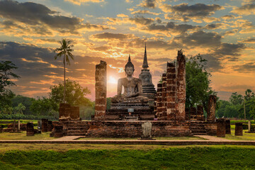 Buddha statue and pagoda Wat Mahathat temple with dramatic syk sunset, Sukhothai Historical Park, Thailand