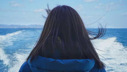 The back of a woman looking out to sea from a boat.