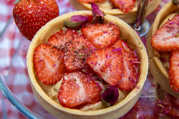 A strawberry tart topped with red flower on a kitchen table cover