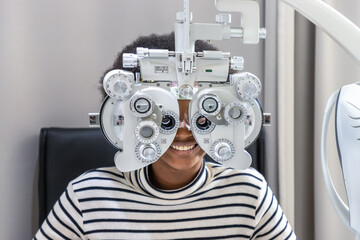 African young woman girl doing eye test checking examination in clinic or optical shop, sitting at phoropter equipment. Eyecare concept.