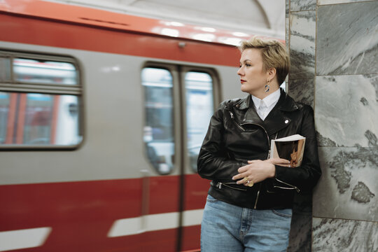 short haired caucasian woman wearing leather jacket on platform of metro station in Saint-petersburg, Russia. Coming train on background. Image with selective focus and noise effect