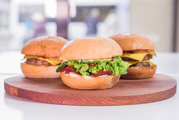 Three different large and juicy burgers on a wooden tray in a restaurant