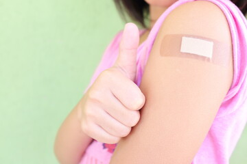 Closeup of shoulder of a vaccinated young Asian girl with adhesive bandage in thumbs up. Young...