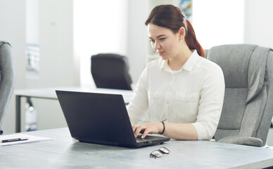 Young attractive business woman working in office smiling looking into laptop
