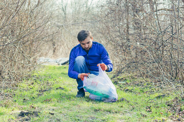 Naklejka na ściany i meble Male park worker collects garbage and plastic in the forest, in the spring, takes care of the ground and trees