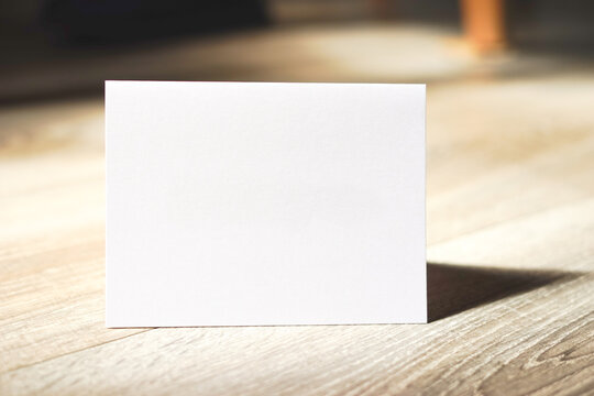 Blank white card standing on wooden table. Modern minimalist composition. Empty space for text. Copy space.