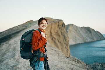 happy traveler woman resting in the mountains near the sea and back view of a model backpack