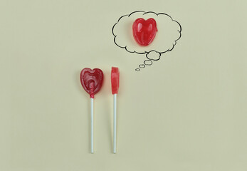 Two heart-shaped lollipops on a brown background, one thinking about another heart that makes his...
