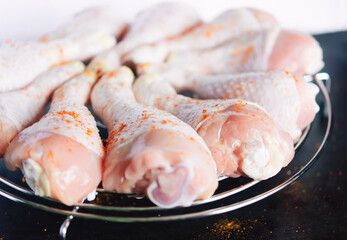 Raw chicken legs with spices on a round metal grill on a dark metal background with space for text. View from above