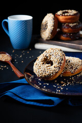 Donuts with chocolate glaze and waffle crumbs on a blue plate with a blue napkin, a blue mug, and wooden spoon on a black background.